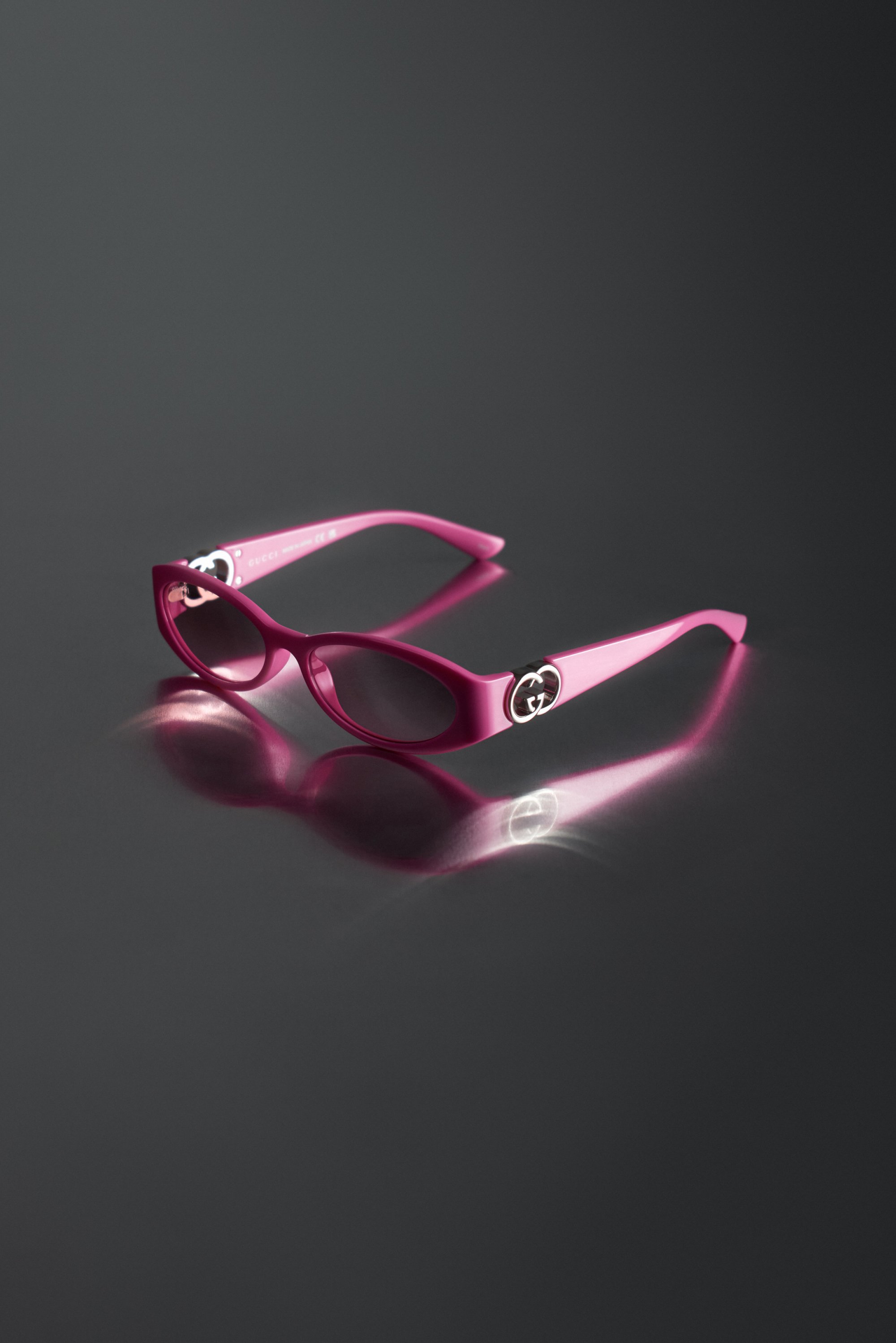 Pink sunglasses with sleek design and Gucci logo on the sides, displayed against a dark reflective background.