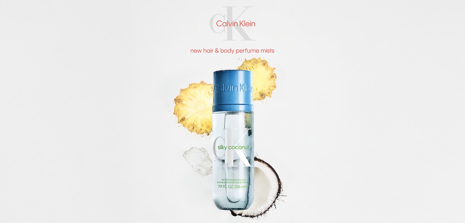 Calvin Klein silkeagtig kokos hår- og kropsparfume sprayflaske med ananasskiver og en halveret kokosnød på en hvid baggrund.