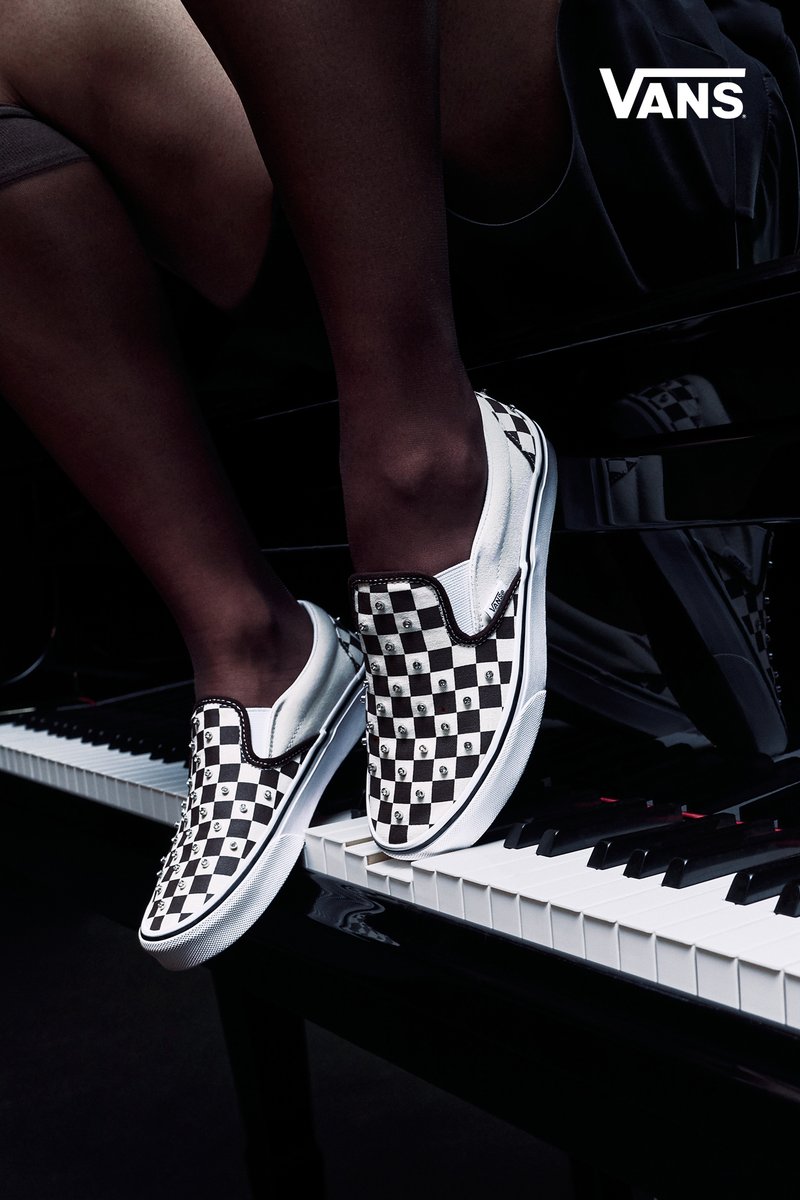 Personne portant des Vans à damier noir et blanc assise sur un piano, les pieds reposant sur les touches, logo Vans dans le coin.