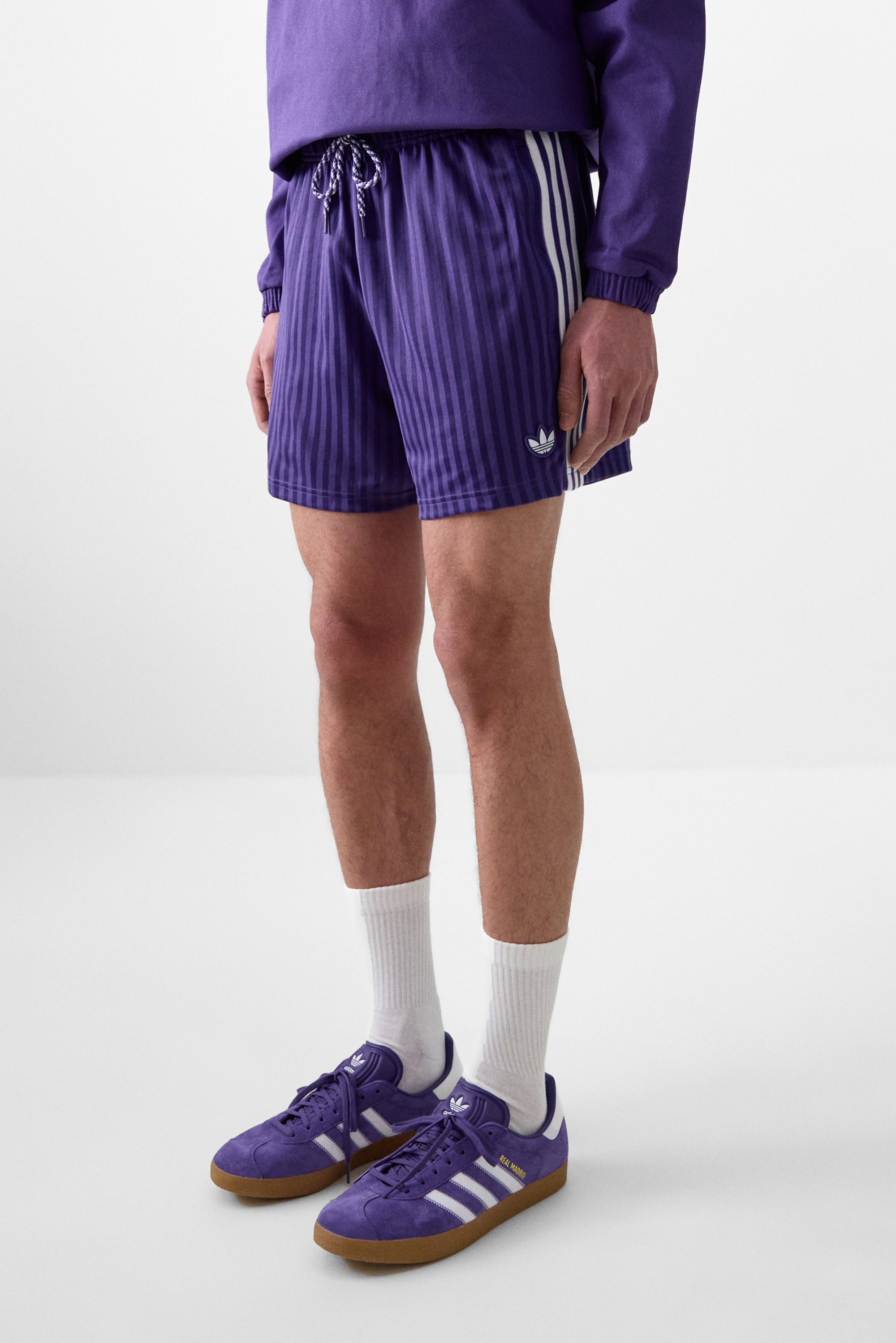 Paarse gestreepte sportshorts met een elastische tailleband, witte trekkoord en wit Adidas-logo. Gecombineerd met paarse sneakers en witte sokken.