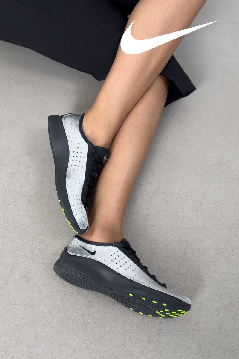 Sports shoes featuring a silver and black synthetic upper, a perforated design, black laces, and vibrant green accents on the sole.