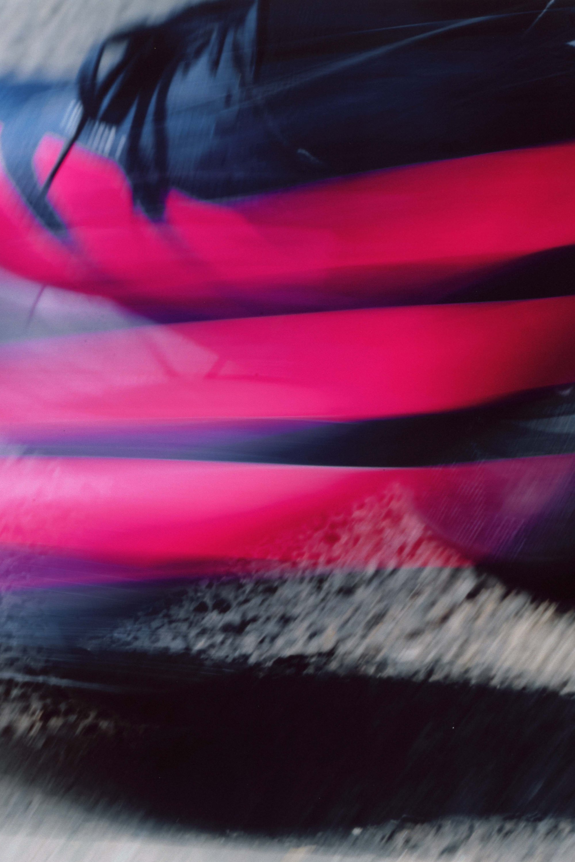 Pink and black running shoes in motion, showcasing a sleek design with textured laces against a blurred background.