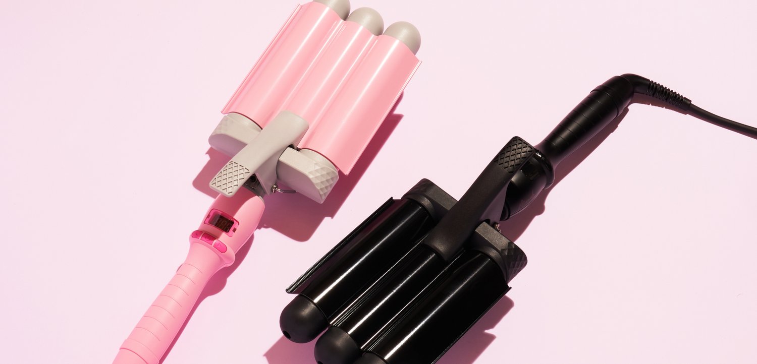 Deux bigoudis triple-baril, un rose et un noir, placés côte à côte sur un fond rose clair.
