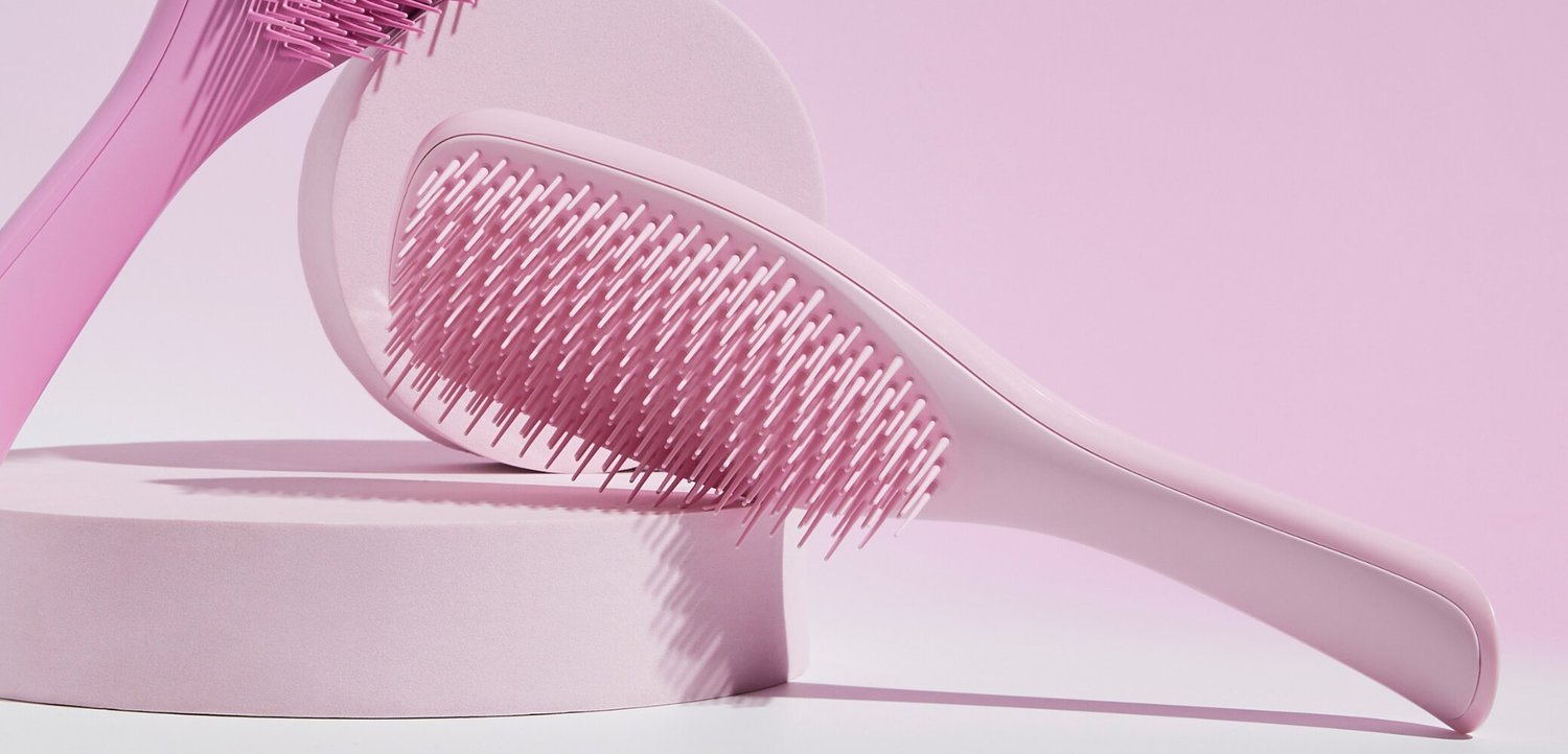 Due spazzole per capelli rosa con setole di plastica esposte su piattaforme rotonde rosa su uno sfondo rosa.