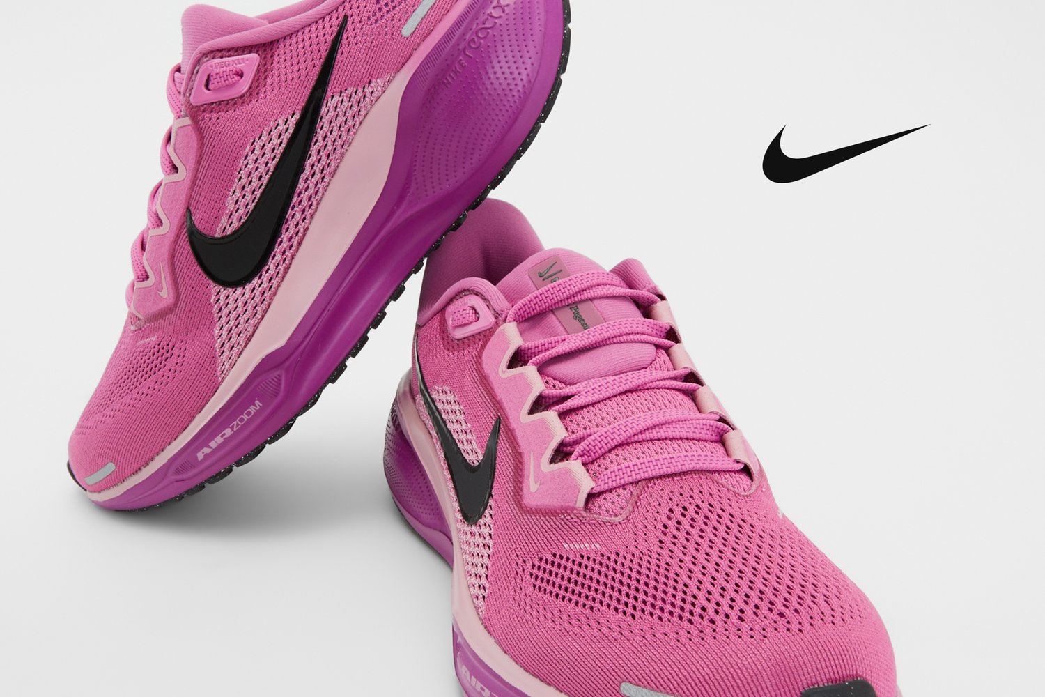 Zapatillas deportivas Nike de color rosa brillante con el logo Swoosh negro, que exhiben un diseño de malla. Una de las zapatillas está en ángulo para mayor visibilidad.