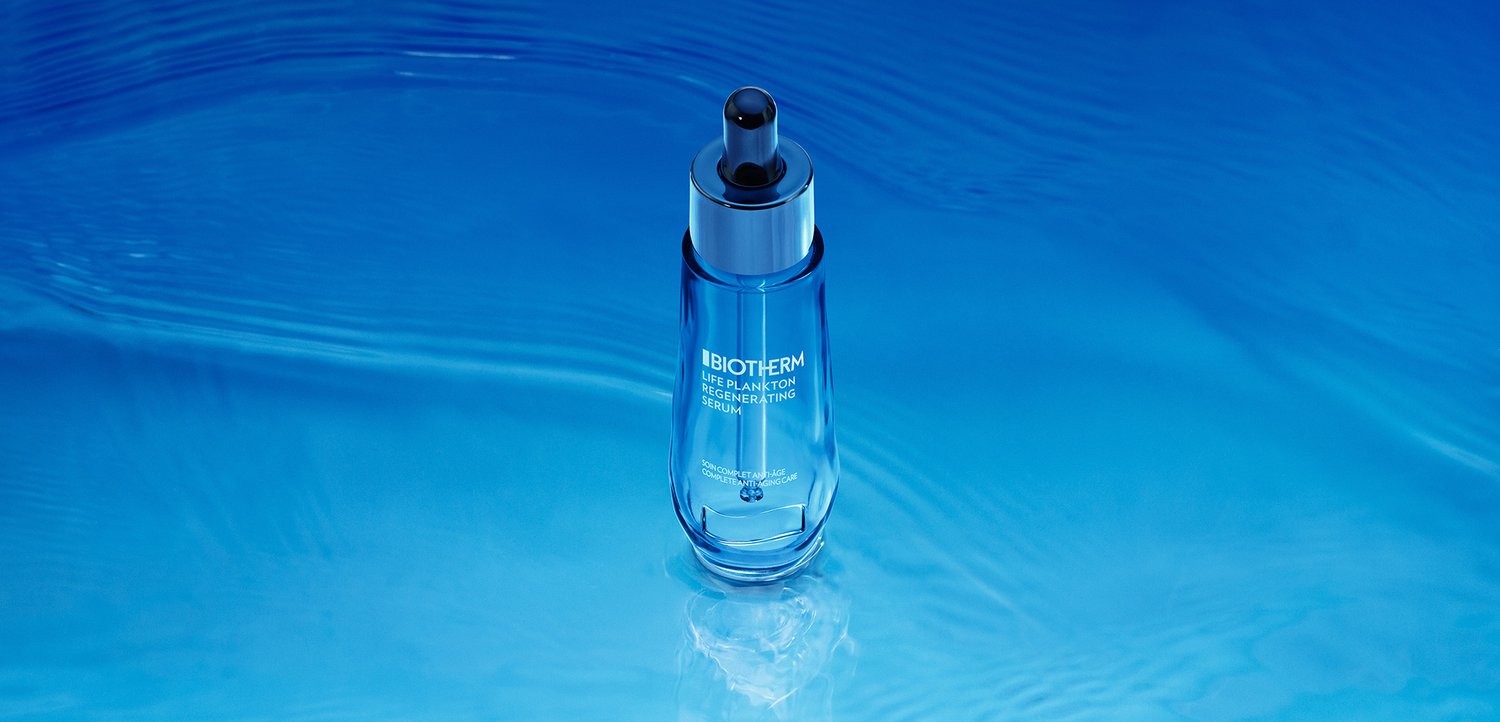 Un flacon de sérum bleu avec un compte-gouttes repose sur une surface bleue ondulante, réfléchissant la lumière et soulignant un thème aquatique serein.
