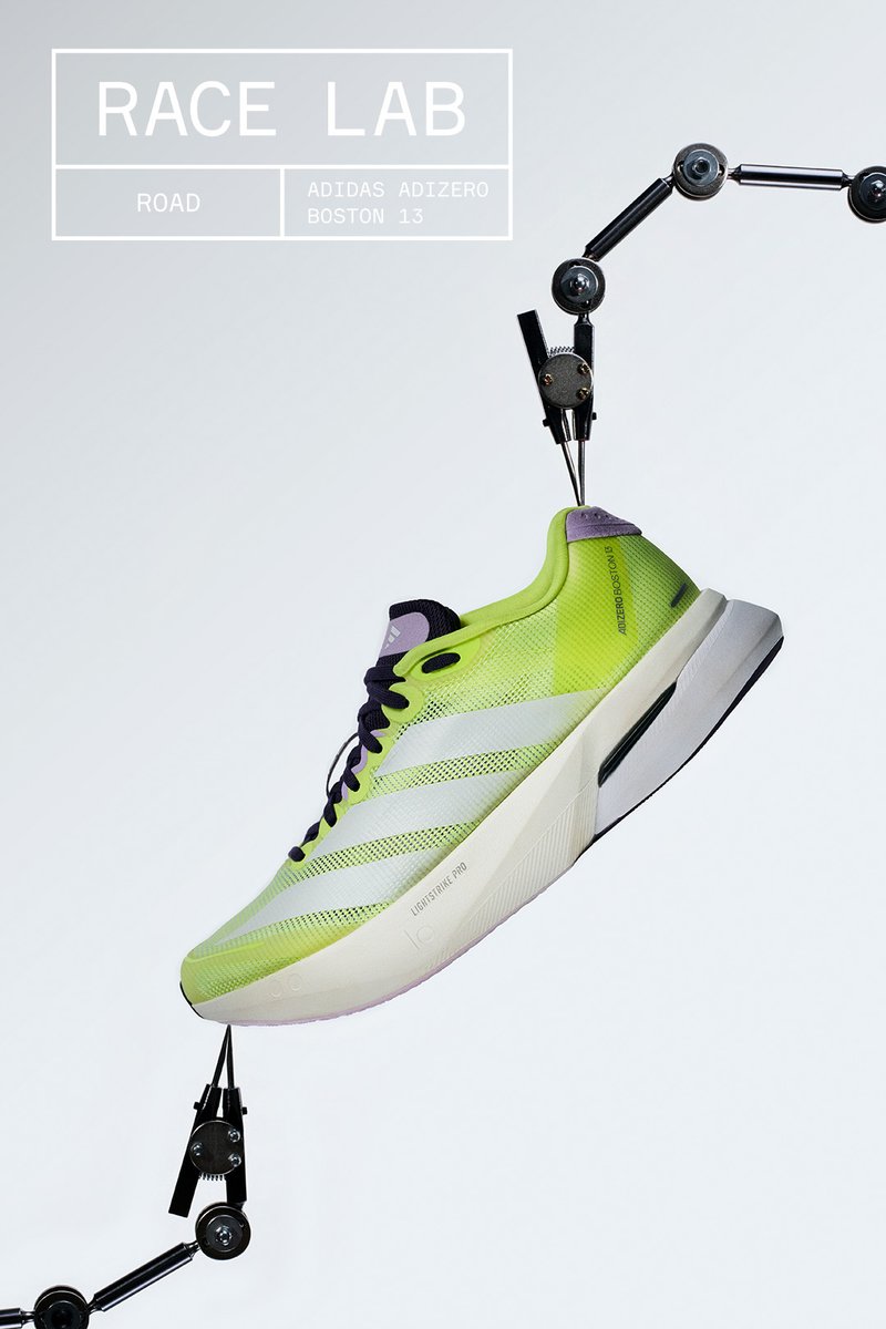 Neonowo zielony i biały but do biegania Adidas Adizero Boston 13 trzymany przez czarne mechaniczne ramiona na jednolitym jasnoszarym tle.