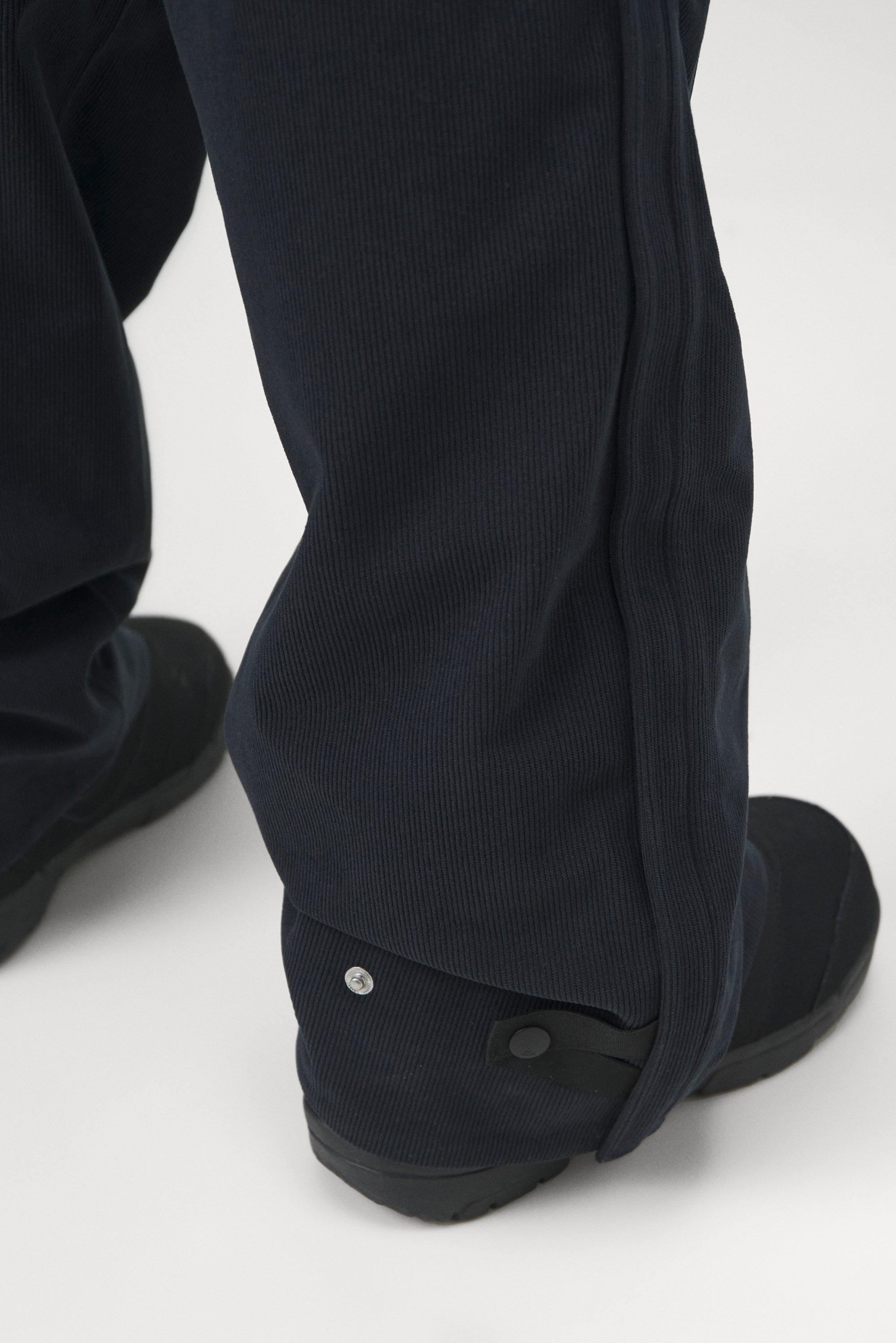 Navy corduroy pants feature close-up view of the legs and black footwear, showcasing buttons and seams along the side.