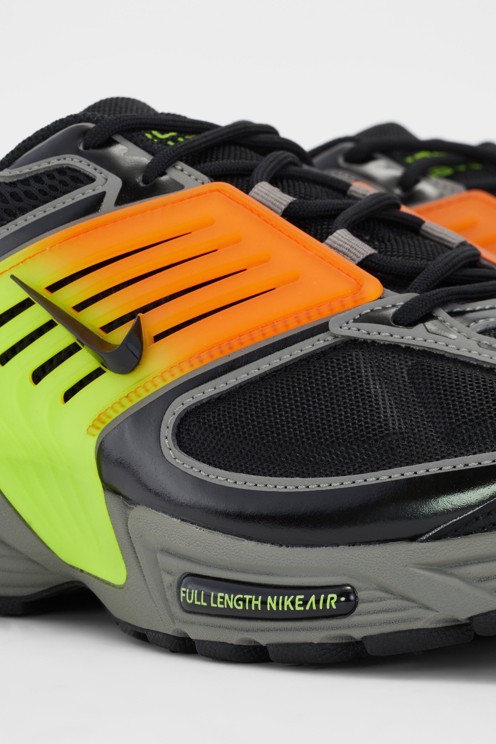 Sneaker met een zwarte mesh bovenkant, heldere oranje en groene accenten, en een "FULL LENGTH NIKEAIR" label op de zijkant. Prominent zichtbaar Nike-logo.