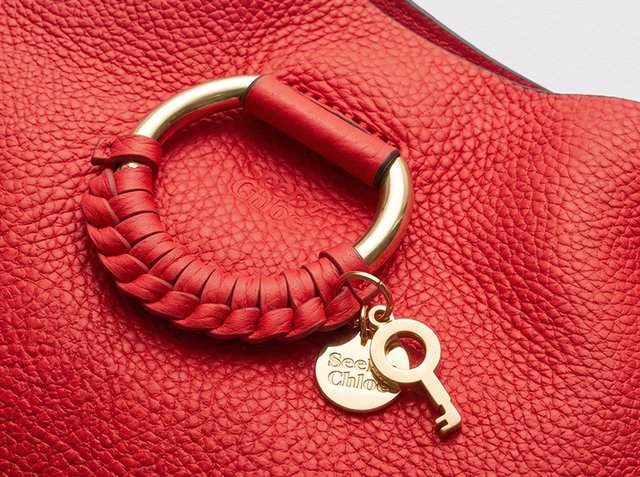 Borsa in pelle rossa texturizzata con manico circolare dorato, dettaglio in pelle intrecciata e targhette dorate a forma di chiave e rotonde incise con "See by Chloé."