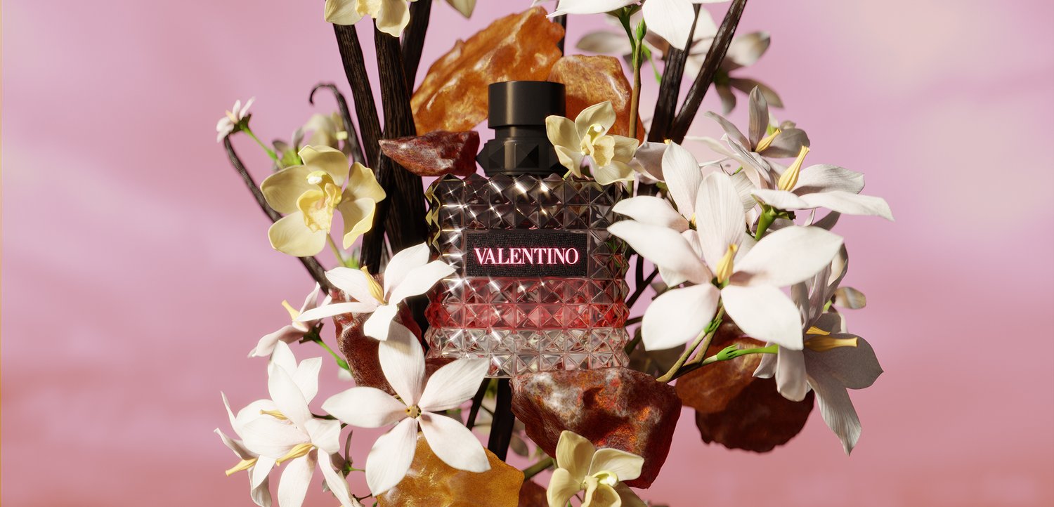 Valentino parfumflesje omringd door witte en gele bloemen met bruine bladeren tegen een zachte roze achtergrond.