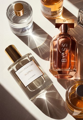 Deux flacons de parfum sur une surface blanche : un flacon en verre transparent avec un bouchon doré étiqueté "ZARKOPERFUME Inception" et un flacon hexagonal teinté de rose avec "BOSS" en relief.