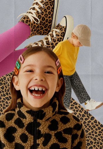Ragazza sorridente con fermagli per capelli colorati e felpa con stampa leopardata, ragazzo in camicia gialla e cappellino che scende, sneakers con stampa leopardata e calzini rosa brillante.