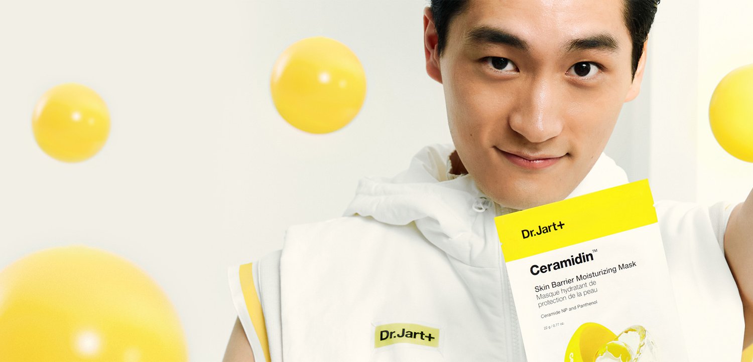 Weiße Verpackung mit gelbem Etikett. Das Produkt trägt die Aufschrift "Dr.Jart+ Ceramidin Skin Barrier Moisturizing Mask." Gelbe Kugeln schweben im Hintergrund.