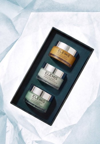 Drei Elemis Pro-Collagen Hautpflege-Tiegel – Reinigungsbalsam, Marine-Creme mit LSF 30 und Nachtcreme – in einer schwarzen Schachtel auf weißem Stoff angeordnet.