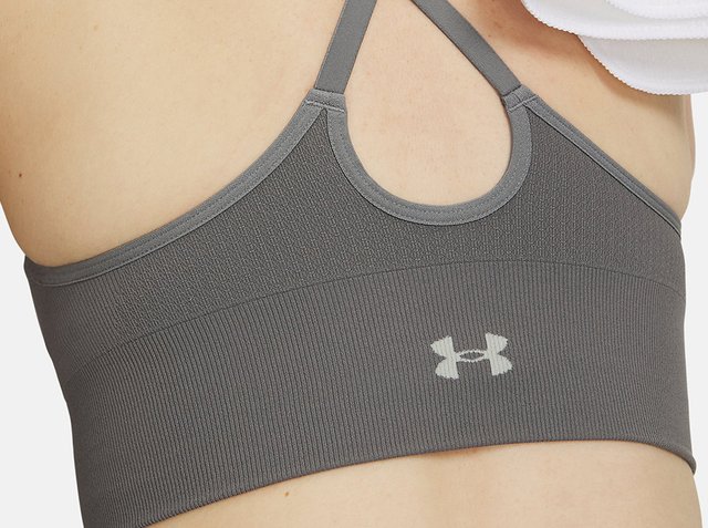 Vista posteriore di una persona che indossa un reggiseno sportivo grigio con sottili spalline e un logo Under Armour al centro della schiena.