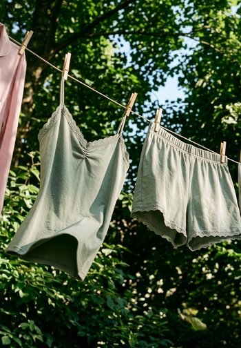 Canottiera verde chiaro e pantaloncini abbinati appesi a una corda per il bucato con mollette in legno, alberi verdi sfocati sullo sfondo.
