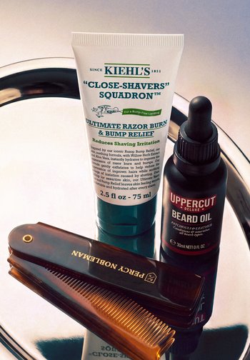Crème apaisante contre les irritations de rasage Kiehl’s, huile à barbe Uppercut Deluxe et peigne pliant Percy Nobleman sur un plateau argenté réfléchissant.