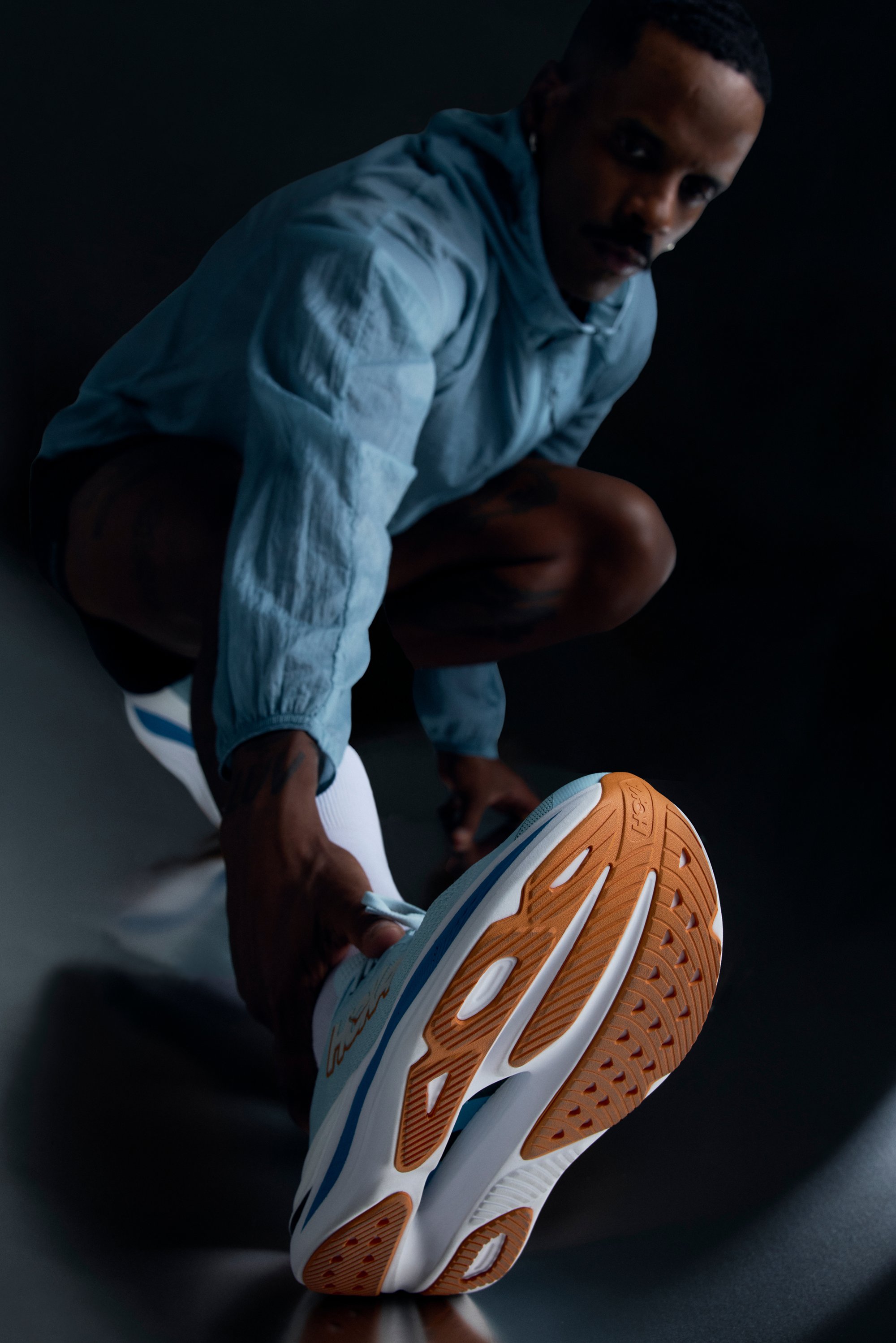 Hellblaue Laufschuhe mit weißer und orangefarbener Sohle. Sie verfügen über ein elegantes Design, ein gemustertes Profil und einen bequemen Sitz für optimale Bewegungsfreiheit.