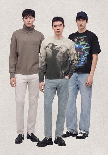 Tre unga män står sida vid sida iklädda lediga kläder med grafiska tröjor och t-shirts, ljusa jeans och svarta skor.