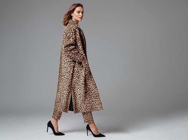 A model walks confidently, wearing a leopard print trench coat and matching pants, paired with black high heels against a neutral background.