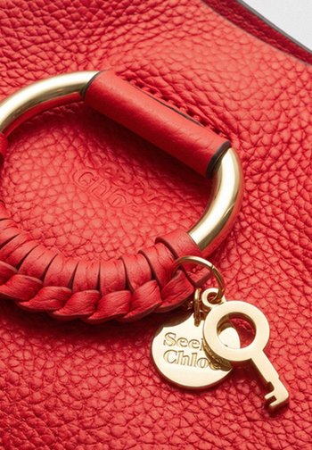 Primer plano de un bolso de mano de cuero rojo texturizado con asa trenzada, anillo dorado y adorno dorado en forma de llave.