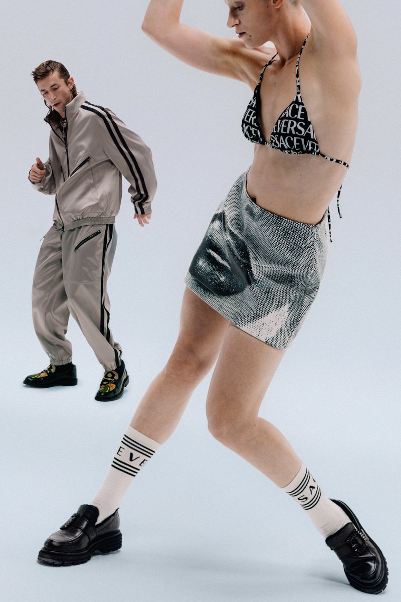 A man in a beige tracksuit and a woman in a black printed bikini and silver skirt strike dynamic poses, showcasing stylish footwear.
