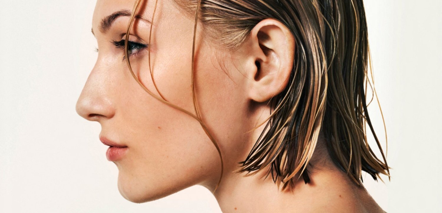 Profile of a woman with wet, short blonde hair looking calmly to the left against a plain light background.