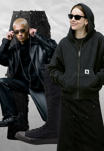 Svart läderjacka och grå hoodie bärs av modeller. Framhävd svart oversized denimkjol och långa svarta snörkängor. Allt i mörka nyanser.