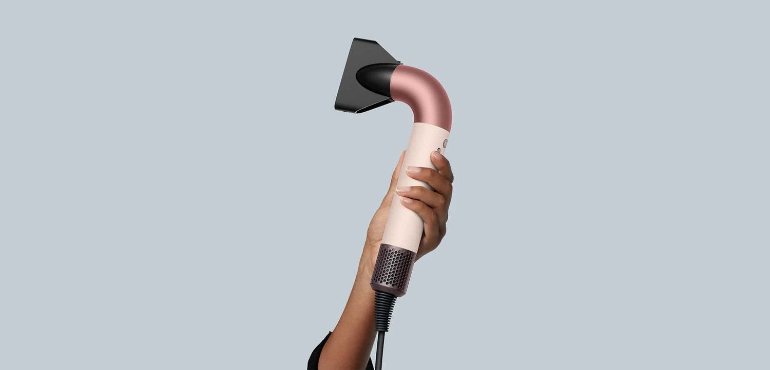 Håndholdt damprenser med et buet rose gold-håndtag, sort dyse og tekstureret greb; fleksibel ledning tilknyttet for nem brug.