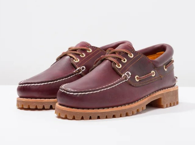 Paire de chaussures bateau en cuir marron avec semelles épaisses en caoutchouc et lacets marron sur une surface blanche contre un fond clair.