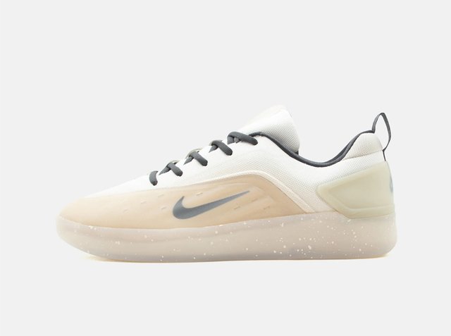 White and beige Nike sneaker with black swoosh, black laces, and speckled translucent sole facing left on plain background.