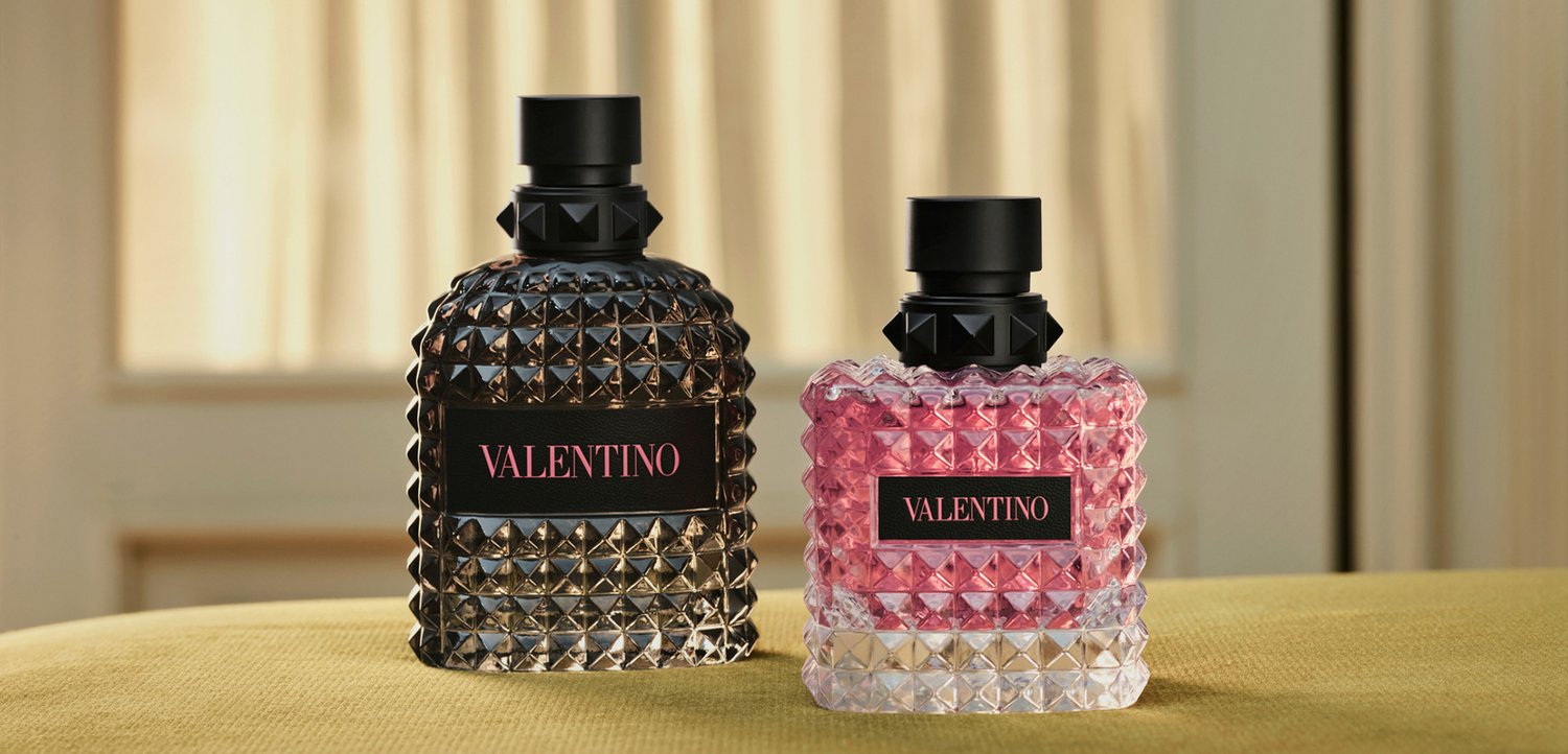 Two Valentino perfume bottles with textured diamond patterns, one black and one pink, placed on a soft green surface indoors.