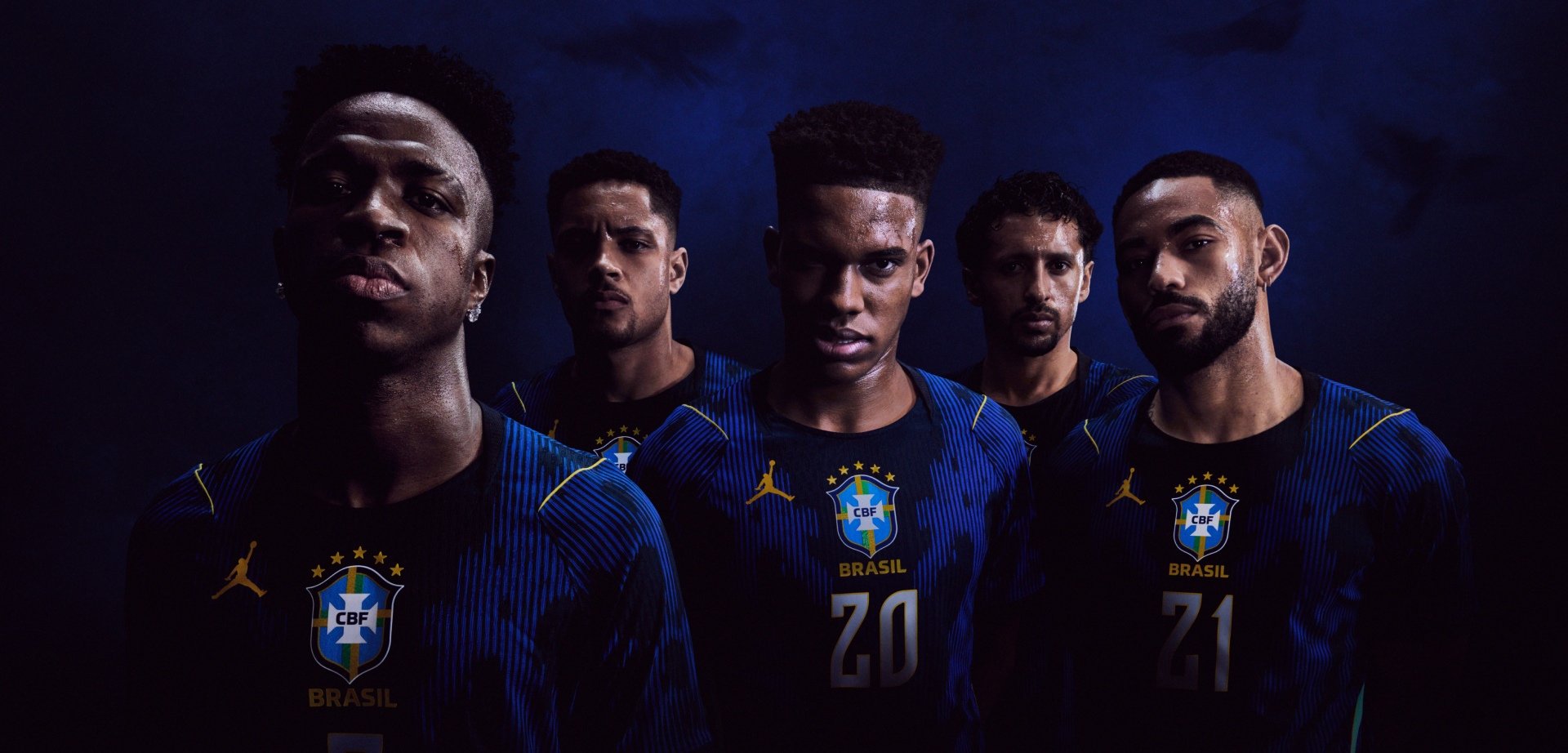 Fünf männliche brasilianische Fußballspieler in dunkelblauen Trikots mit CBF-Logos stehen eng beieinander vor einem dunklen Hintergrund und blicken konzentriert und entschlossen.