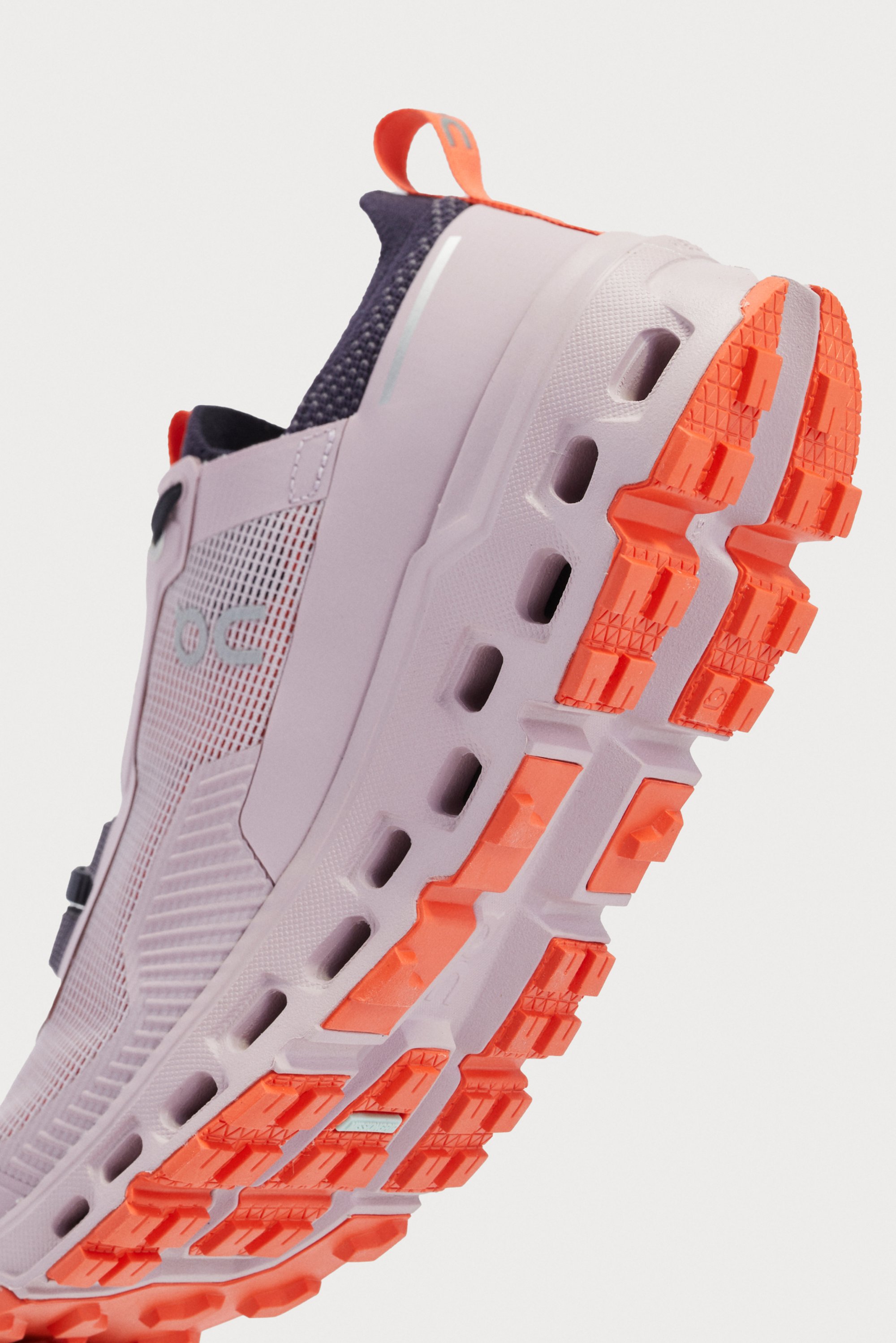 Close-up of a lavender athletic shoe with an orange outsole, showcasing textured tread and mesh detailing on the upper.