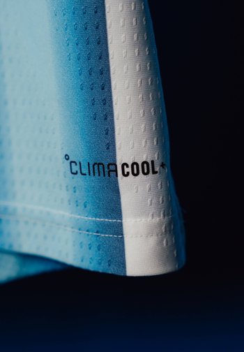 Gros plan de tissu bleu et blanc respirant avec le texte "climacool+" imprimé sur un matériau de vêtement de sport texturé.