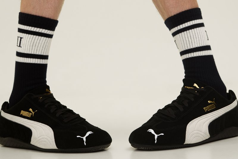 Zapatillas Puma en blanco y negro combinadas con calcetines a rayas en azul marino, sobre un fondo claro. Enfoque en los detalles y el diseño del calzado.