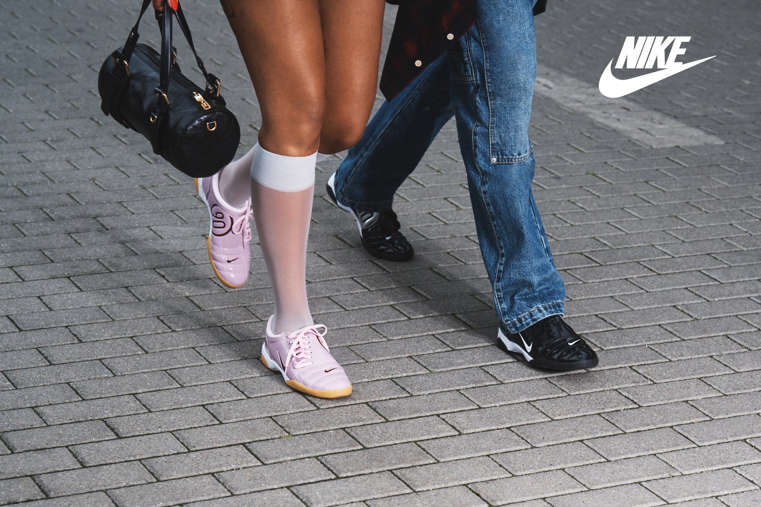 Zapatillas Nike rosas con cordones y acentos negros, llevadas con calcetas blancas hasta la rodilla. Un bolso negro y jeans de mezclilla son visibles en el fondo.