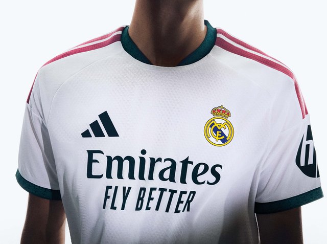 Nahaufnahme einer Person, die ein weißes Real Madrid Fußballtrikot mit den Logos von Emirates Fly Better und Adidas trägt.