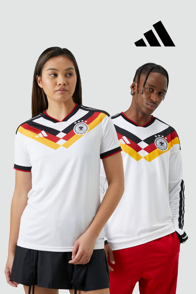 Two models wearing white Germany football jerseys featuring red, yellow, and black geometric accents, standing against a plain background.