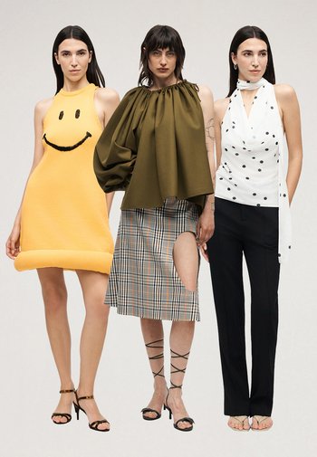 Drie vrouwen staan zij aan zij in modieuze outfits: gele jurk met smileygezicht, olijfkleurige top met pofmouwen en geplooide rok, witte top met stippen en zwarte broek.