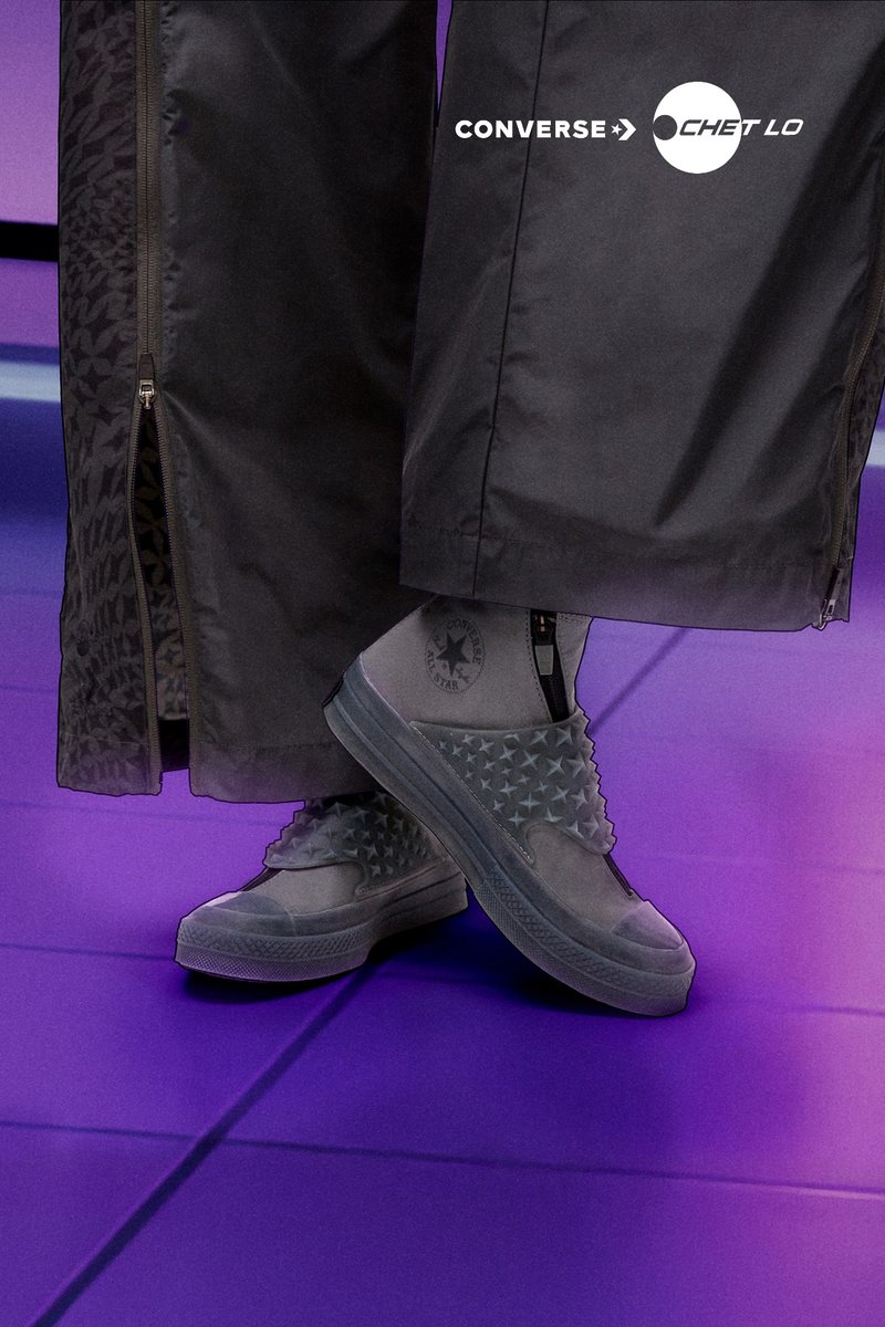 Graue Converse Chet Lo Sneaker zeigen ein strukturiertes Sternenmuster, eine runde Zehenform und glattes Material, kombiniert mit lockeren schwarzen Hosen.