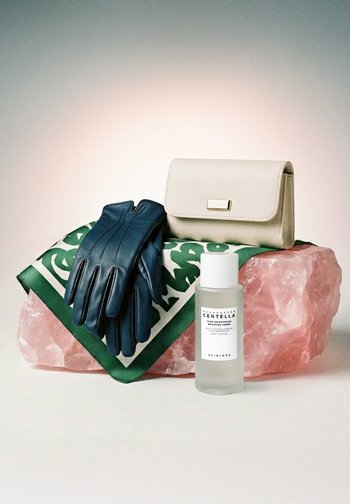 Zwarte leren handschoenen, beige clutch, groene sjaal met patroon op roze kristal, met een doorzichtige fles Madagascar Centella toner.