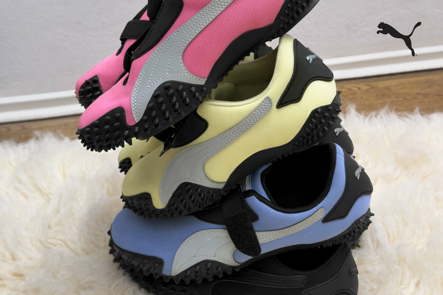 Cuatro pares de zapatillas deportivas apiladas, con colores vibrantes: rosa, amarillo, azul y negro. Fabricadas con un material texturizado y suelas de goma.