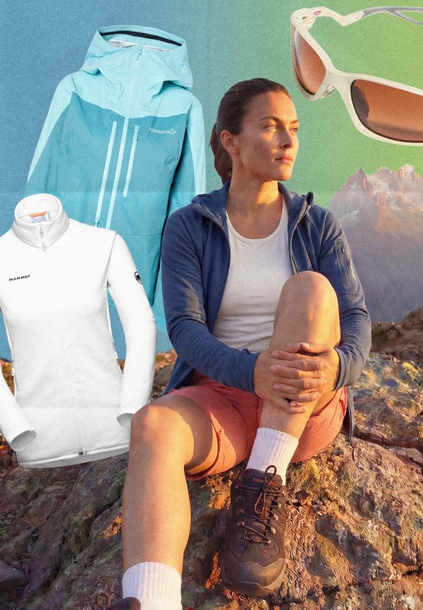 Moteris žygių aprangoje sėdi ant uolėto žemės paviršiaus saulėlydžio metu, šalia kalnų kraštovaizdžio eksponuojami lauko striukės ir saulės akiniai.