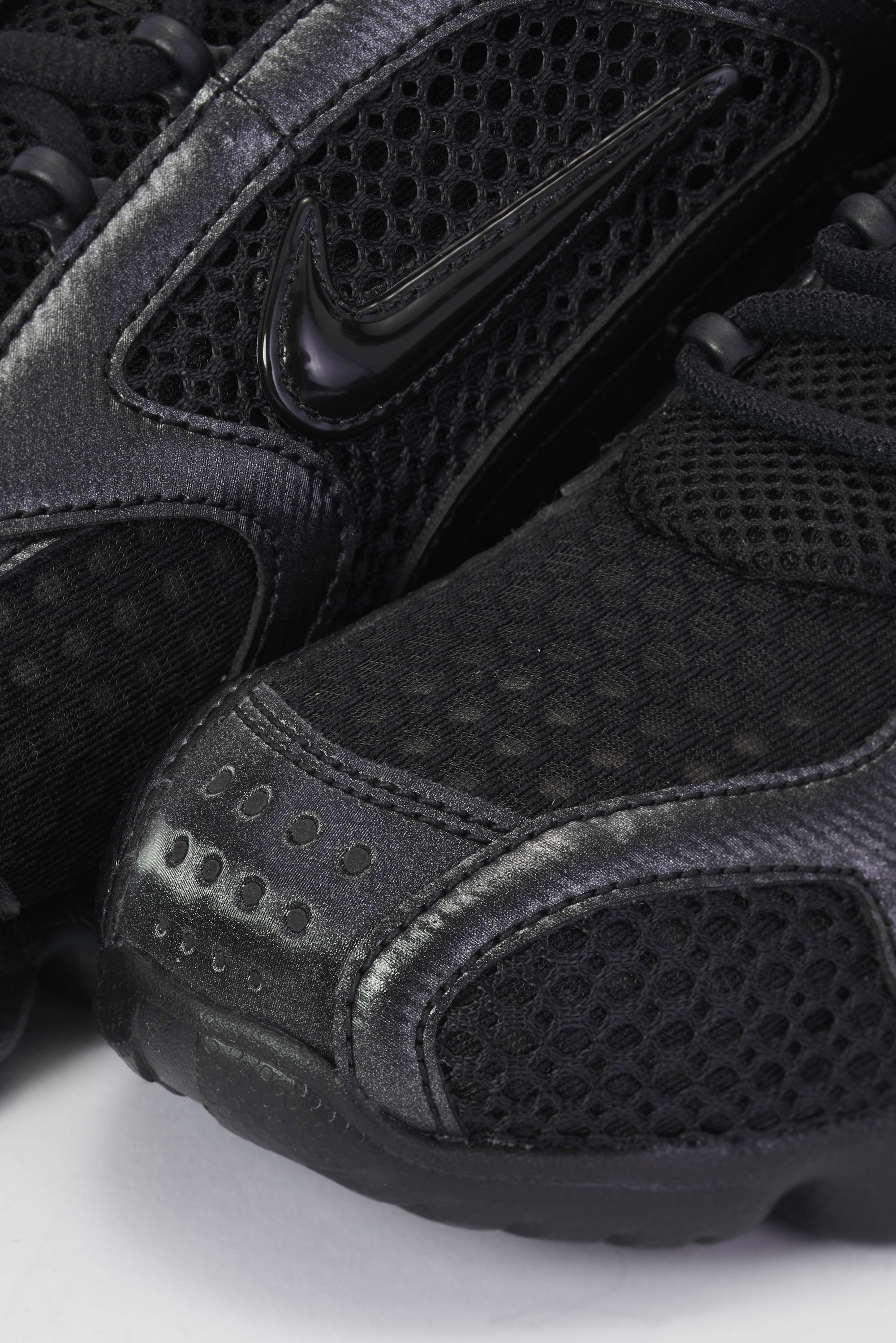 Close-up van zwarte Nike-sneakers met mesh en gladde texturen, met zichtbare veters en logo aan de zijkant.