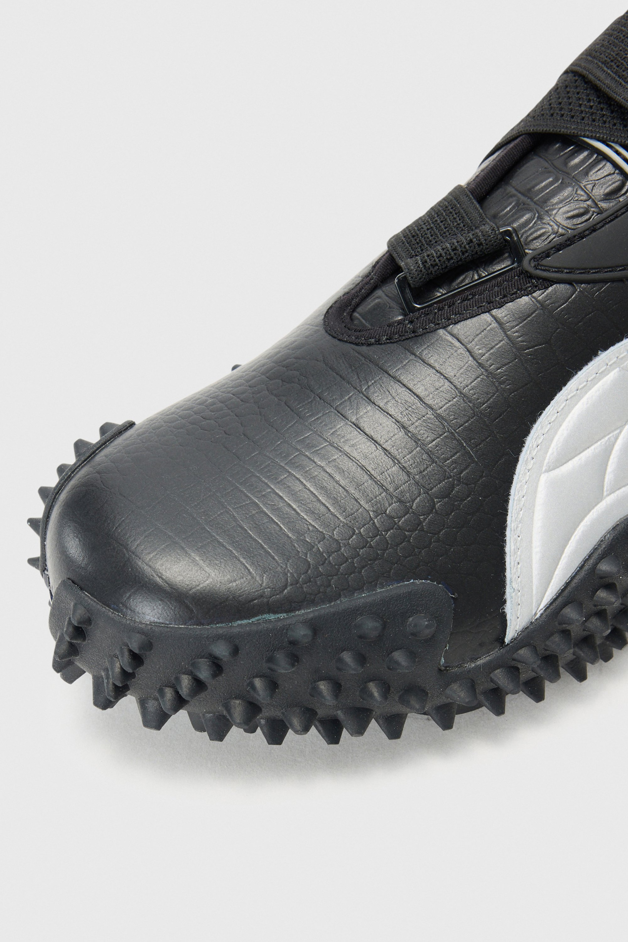 Close-up of a black sports shoe featuring a textured surface and a spiked sole, designed for traction on grass or turf surfaces.