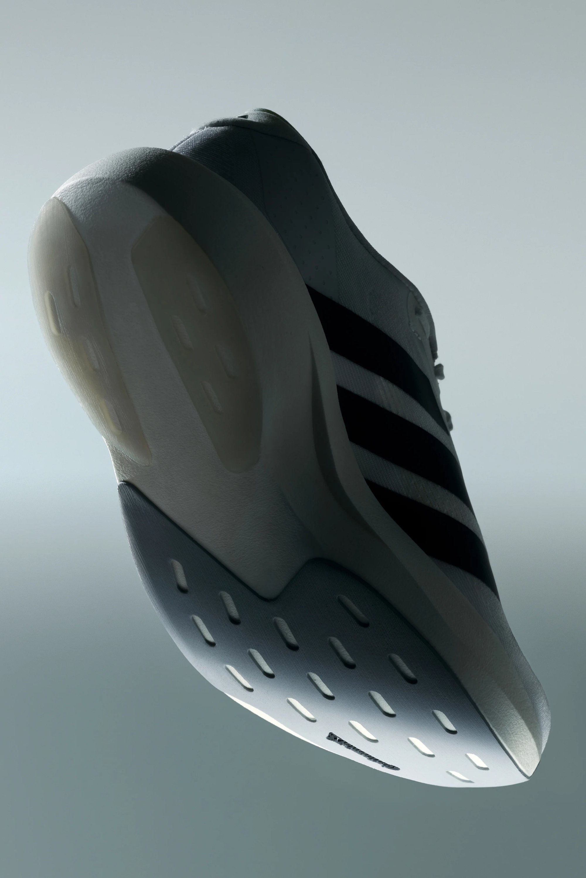 Un primer plano de una zapatilla deportiva de color claro, que muestra su suela texturizada y tres distintivas franjas negras en el costado.