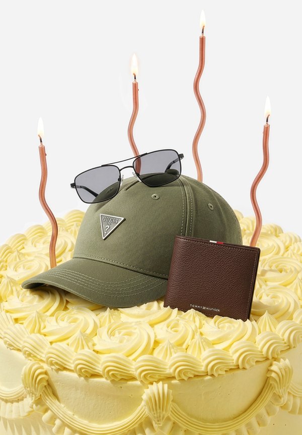Cream-frosted cake topped with an olive green Guess cap, dark sunglasses, a brown Tommy Hilfiger wallet, and four lit wavy candles.