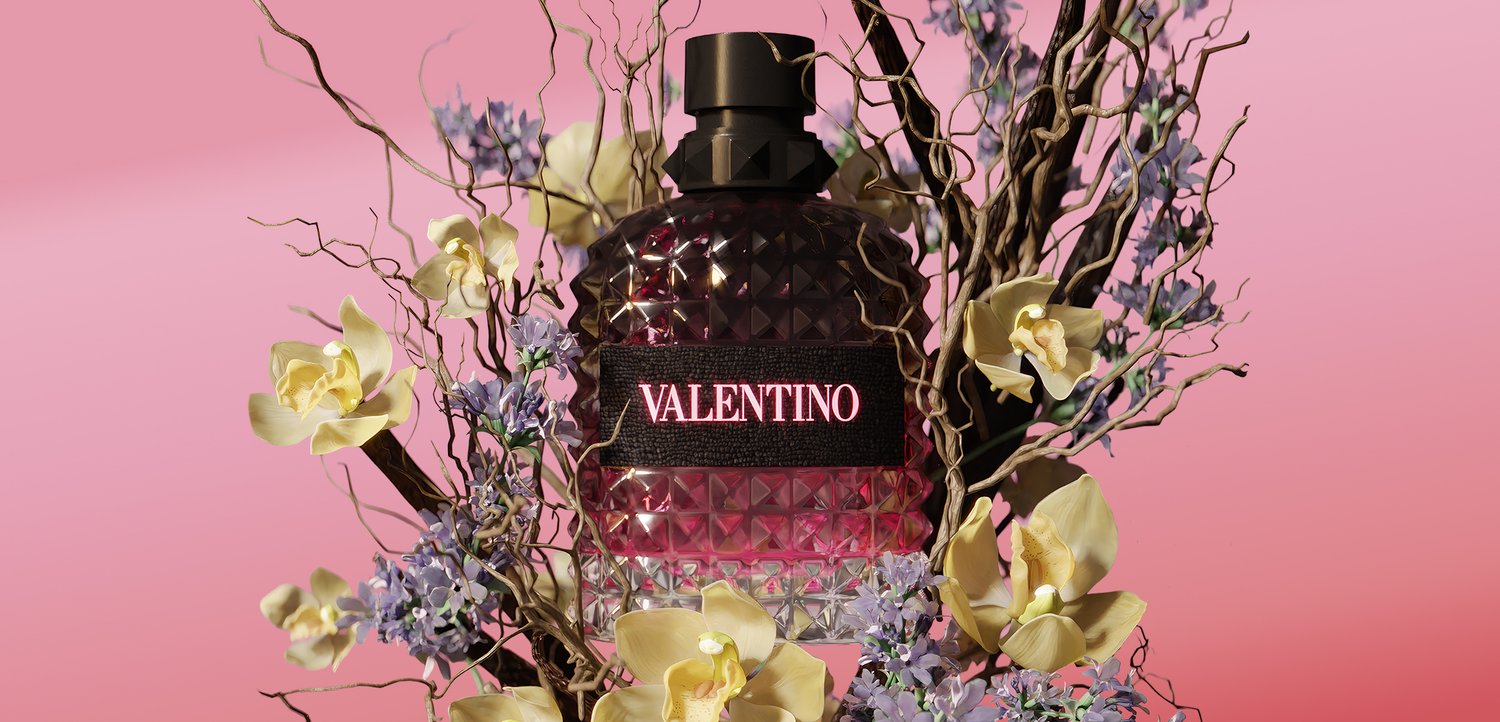 Black and pink Valentino perfume bottle surrounded by pale yellow and purple flowers with twisted branches on a pink background.